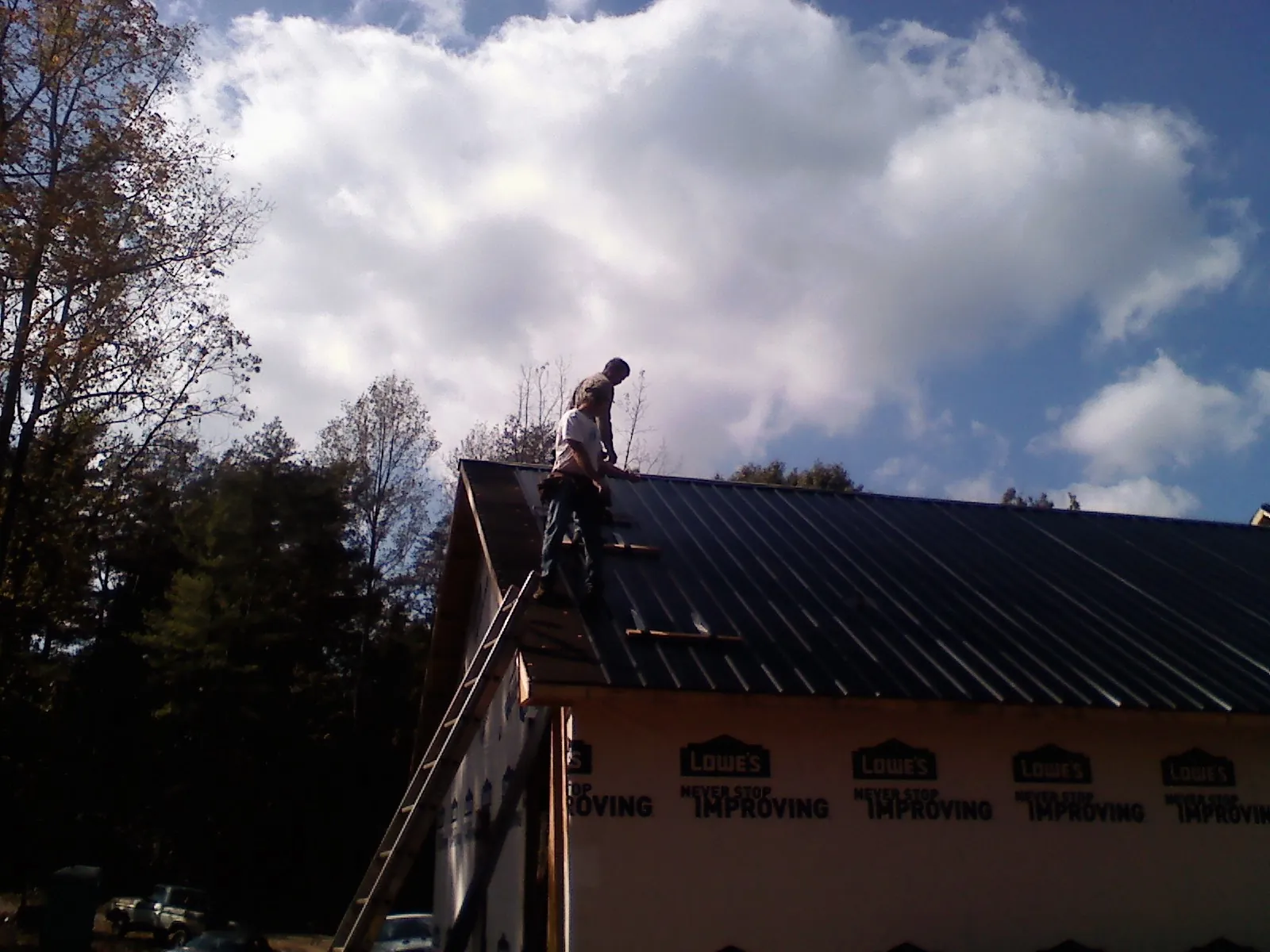 Roofer fastening dark metal panels high against a cloudy sky, from a Roof Inspection job in Cascade